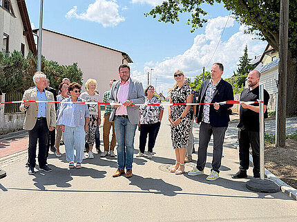 Offizielle Freigabe der grundhaft ausgebauten Zechenstraße in Hohenstein-Ernstthal: Oberbürgermeister Lars Kluge und Projektbeteiligte stehen zum symbolischen Durchschneiden des Eröffnungsbandes auf der neu ausgebauten Straße. Im Hintergrund sind Anwohnerinnen und Anwohner sowie die modernisierte Wohnstraße unter sommerlichem Himmel zu sehen.
