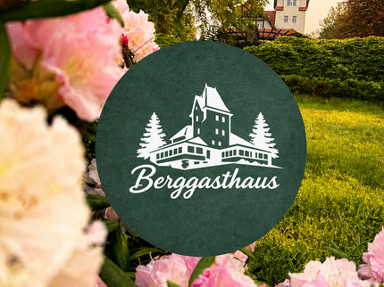 Blühende rosa Rhododendren rahmen den Blick auf das Berggasthaus auf dem Pfaffenberg in Hohenstein-Ernstthal. Im Vordergrund befindet sich ein Schild mit Berggasthaus-Logo, im Hintergrund ist das Gebäude in warmer Abendstimmung zu sehen.