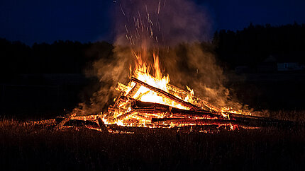 Hexenfeuer mit aufgeschichteten Holzstämmen am 30. April in der Dämmerung.